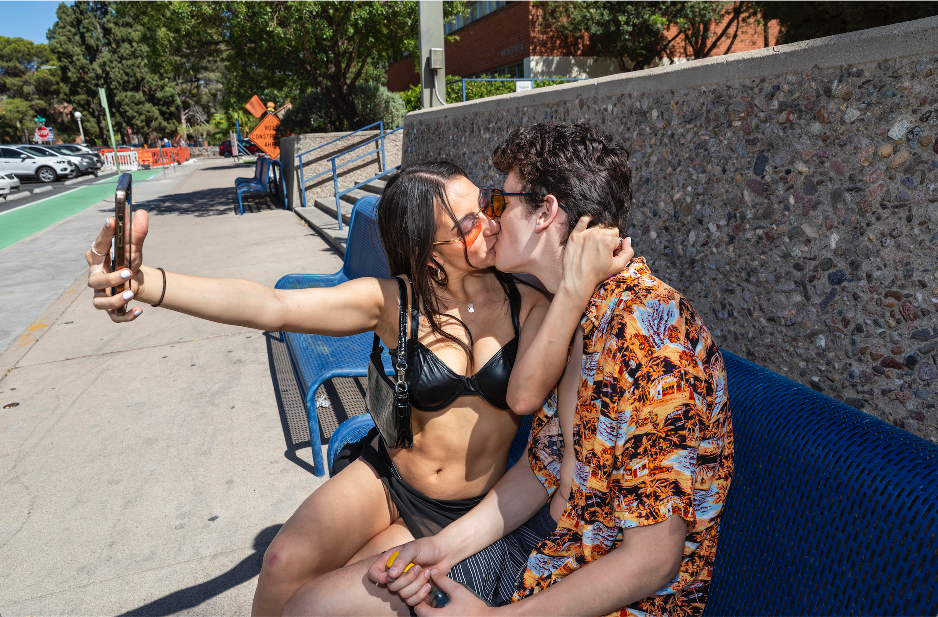 Image of a man and a women in bra and short skirt kissing while taking a selfie