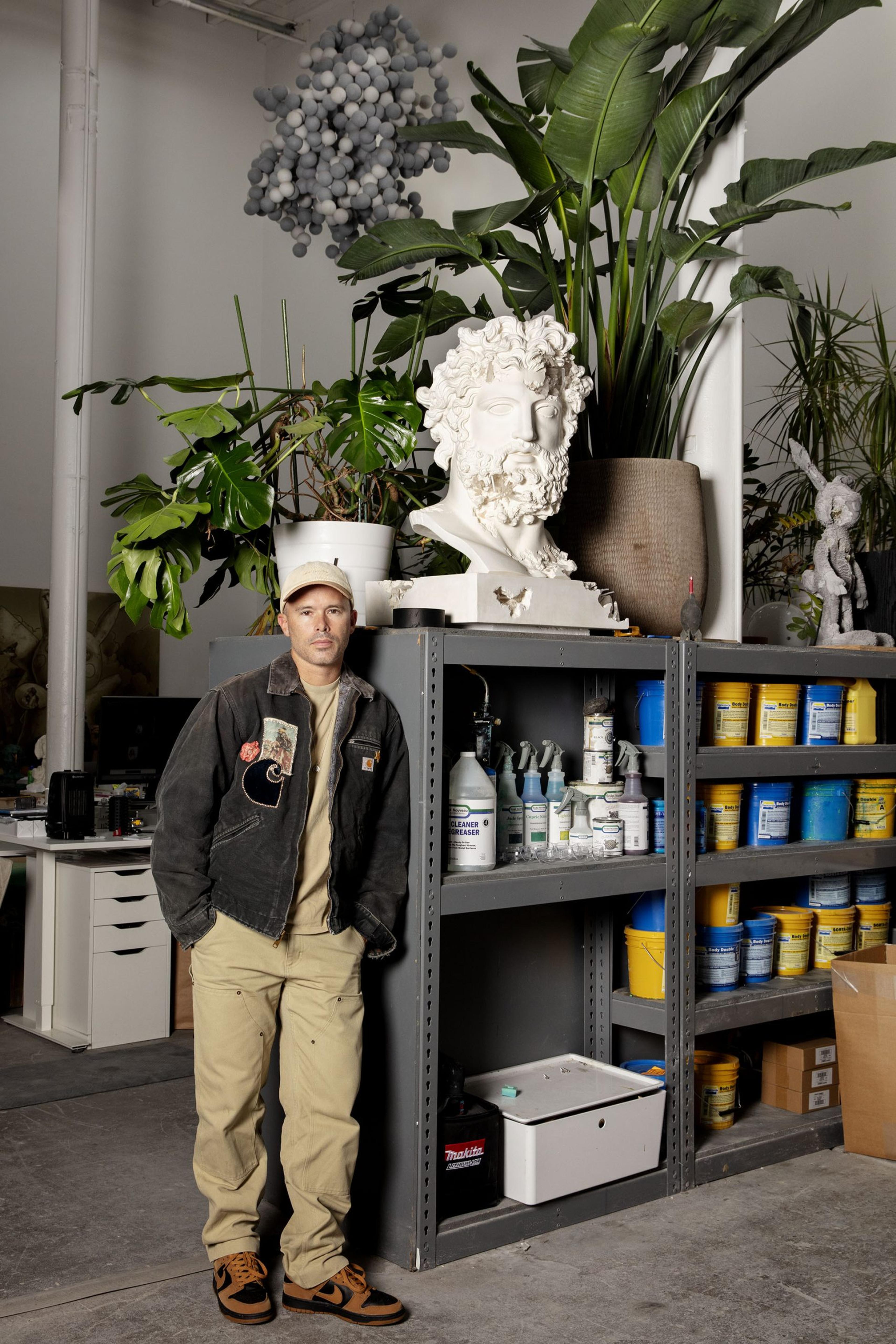 Portrait of Daniel Arsham in his studio, posing next to a shelf of sculptural materials