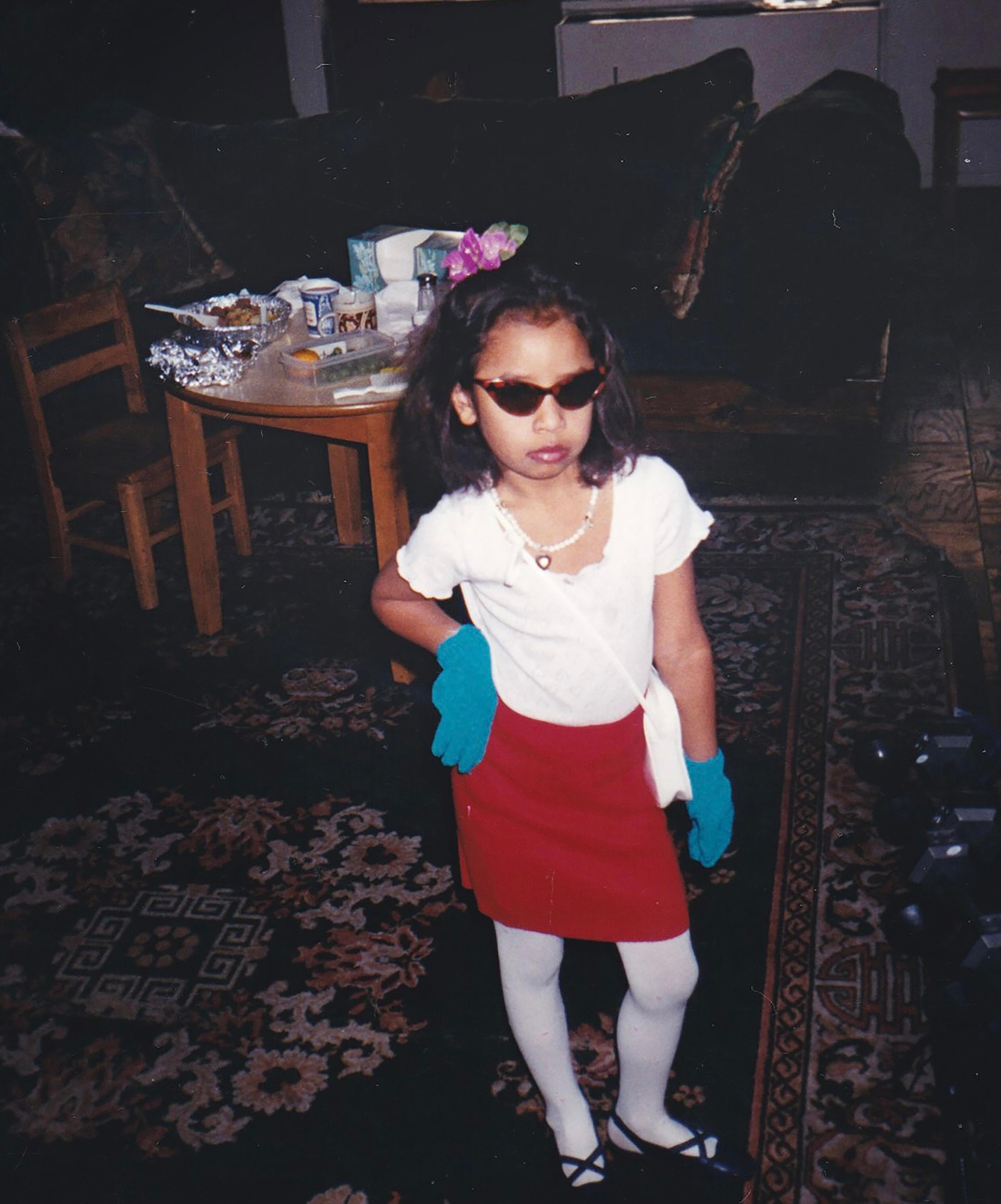 A photograph of a young child wearing sunglasses and posing with her hand on her hip
