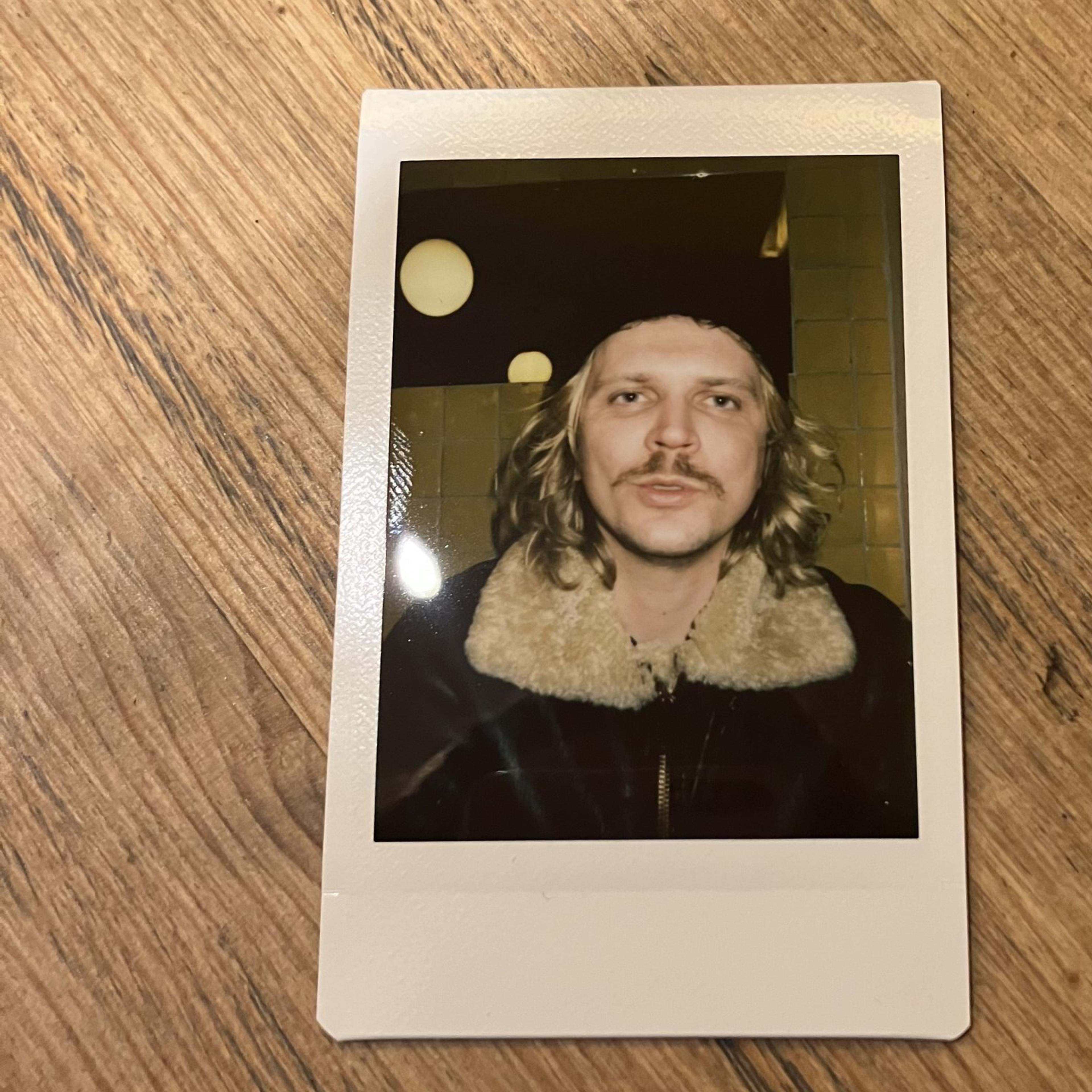 Image on brown wooden table of portrait image of Victor Gustafsson in a lambswool leather jacket and black hat. 