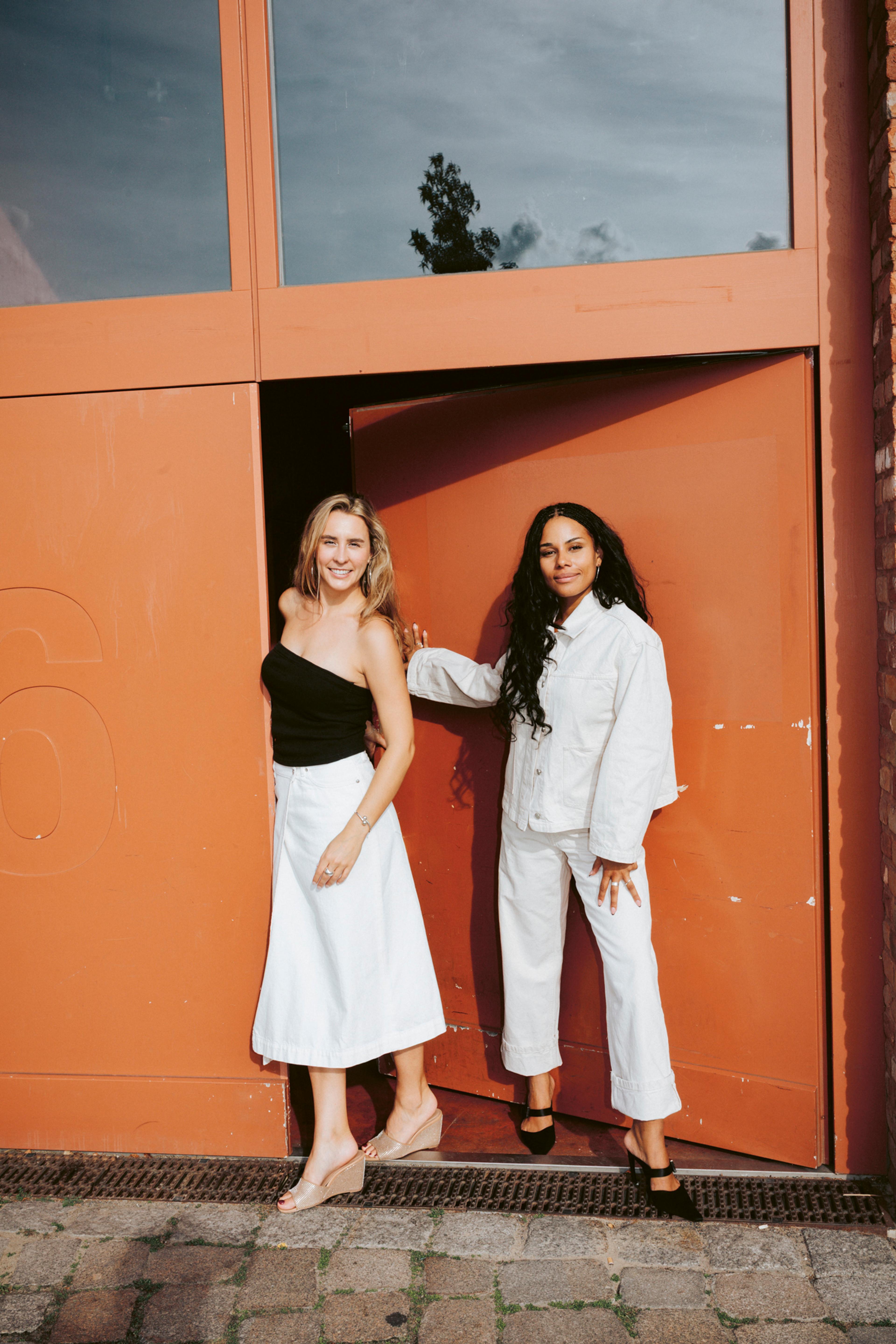 Image of two women, Daria and Cynthia in front of a modern orange door