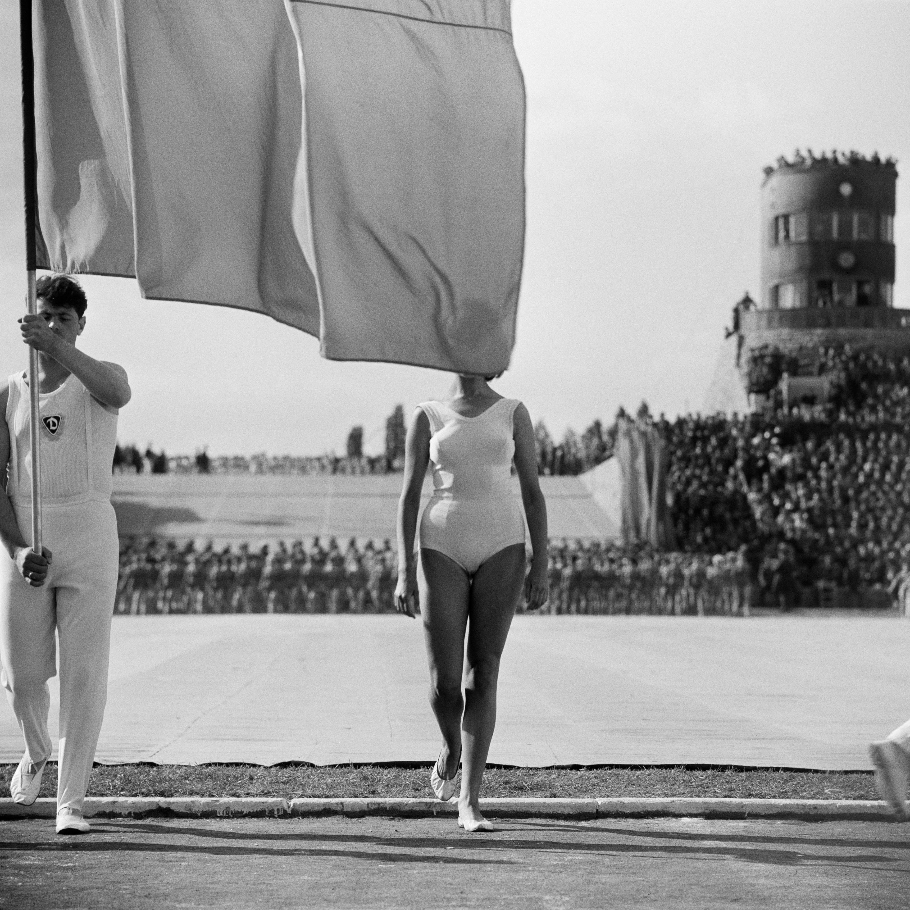 Mann mit weißem Trainingsanzug der eine Flagge hält, die das Gesicht einer Frau verdeckt