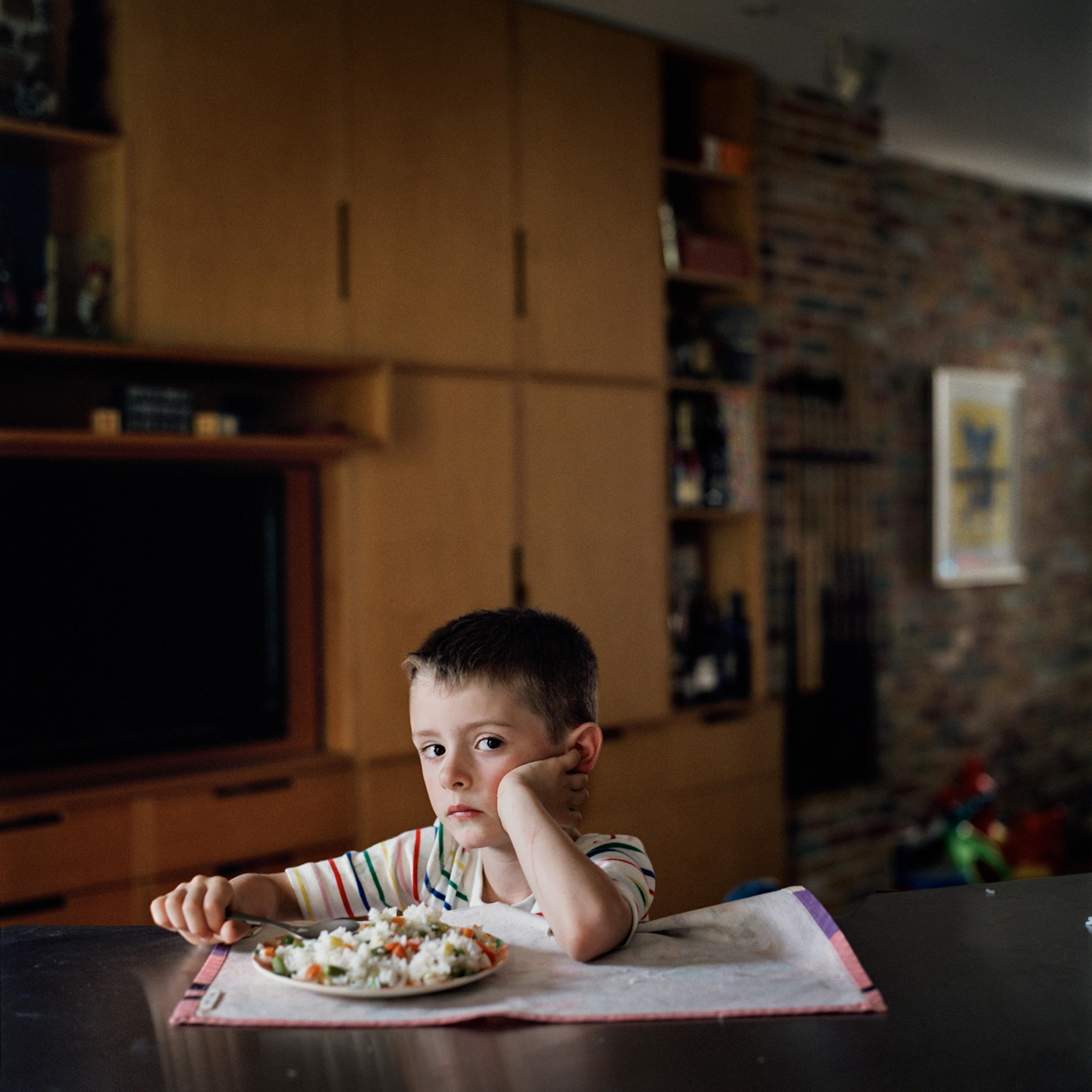 A photograph of a young child sitting at a kitchen table eating a meal