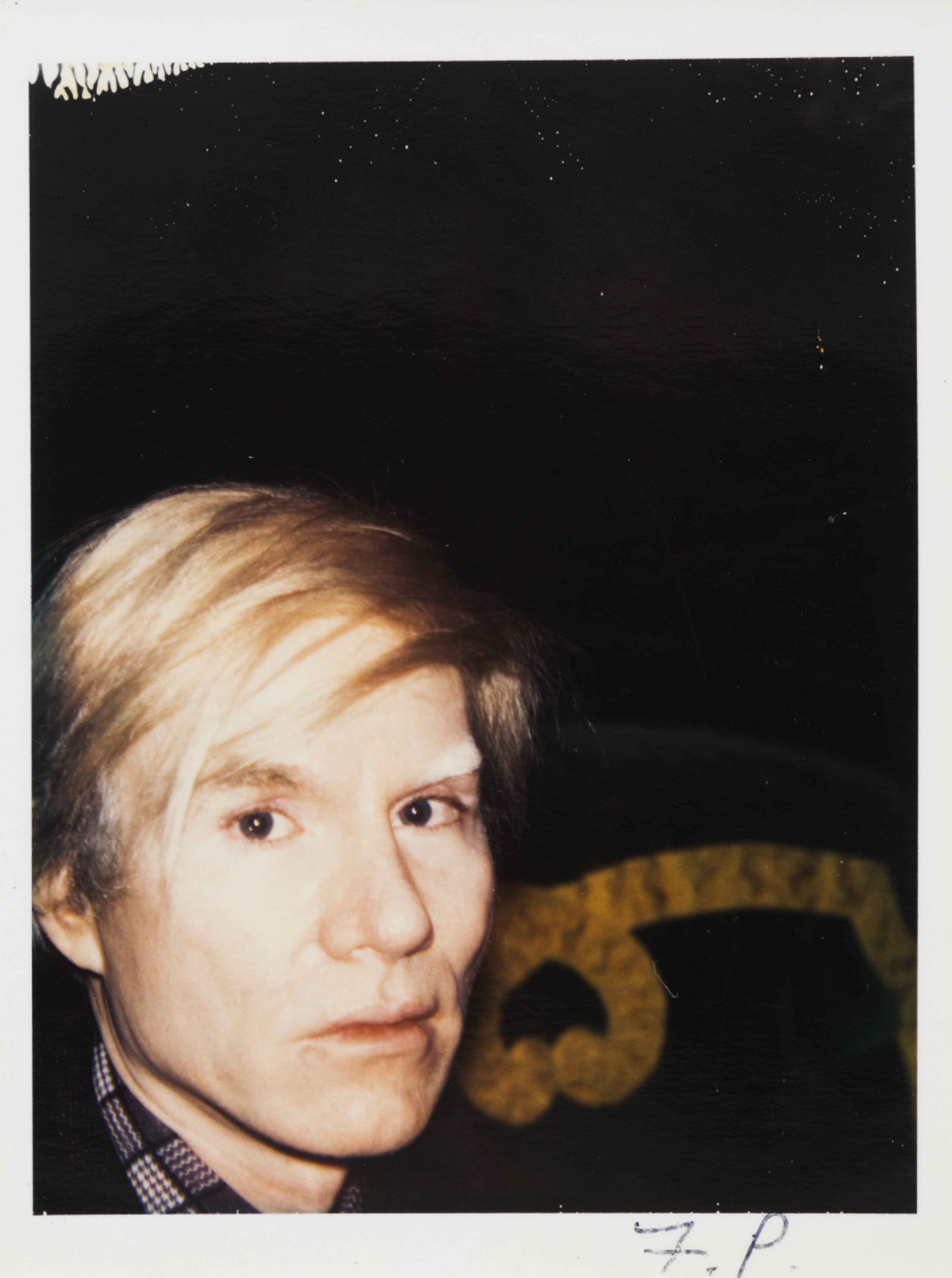 Portrait of Andy Warhol wearing a blonde wig, looking into the camera.