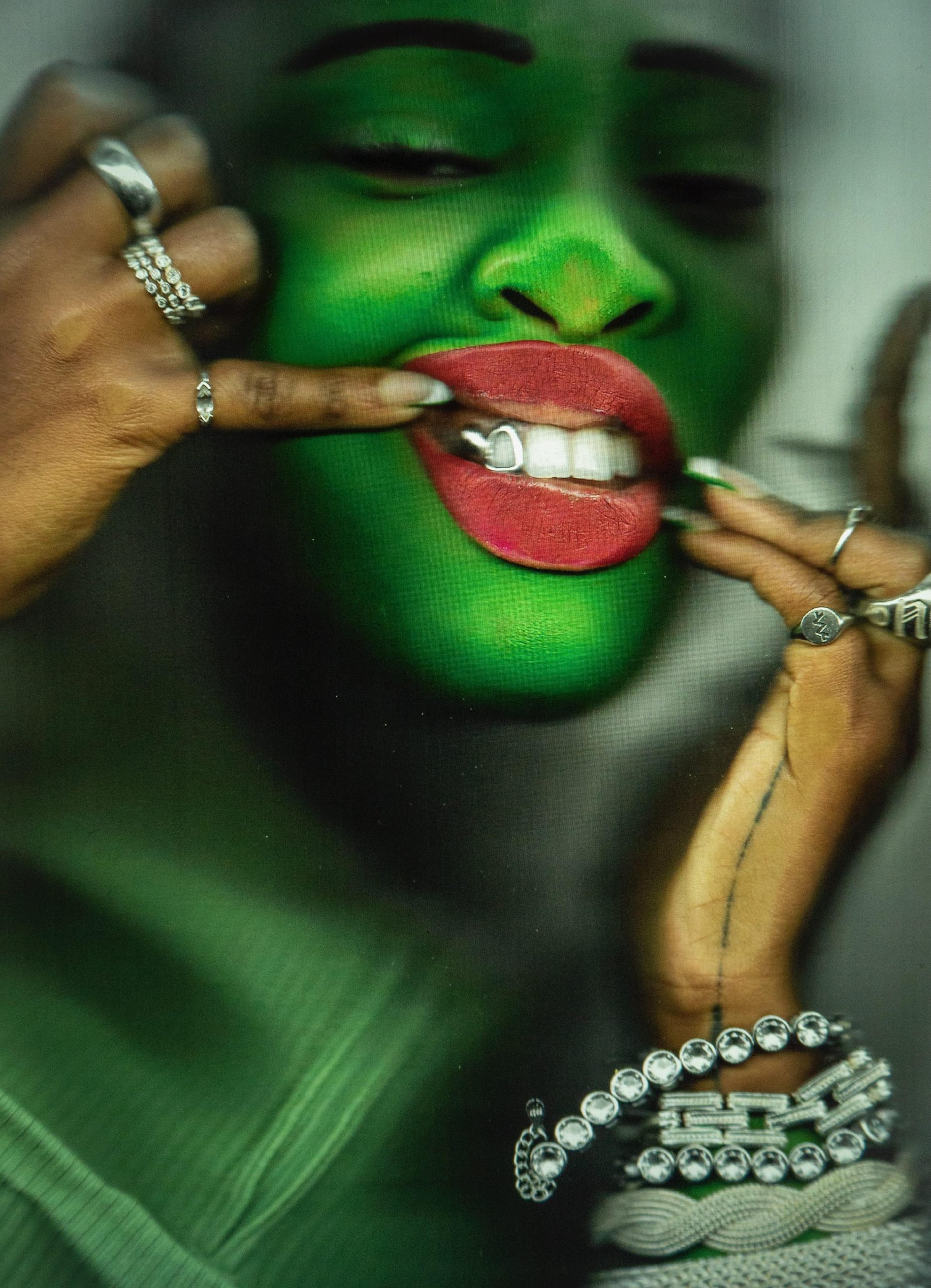A close-up portrait of a woman covered in green paint, pressed up against a clear surface