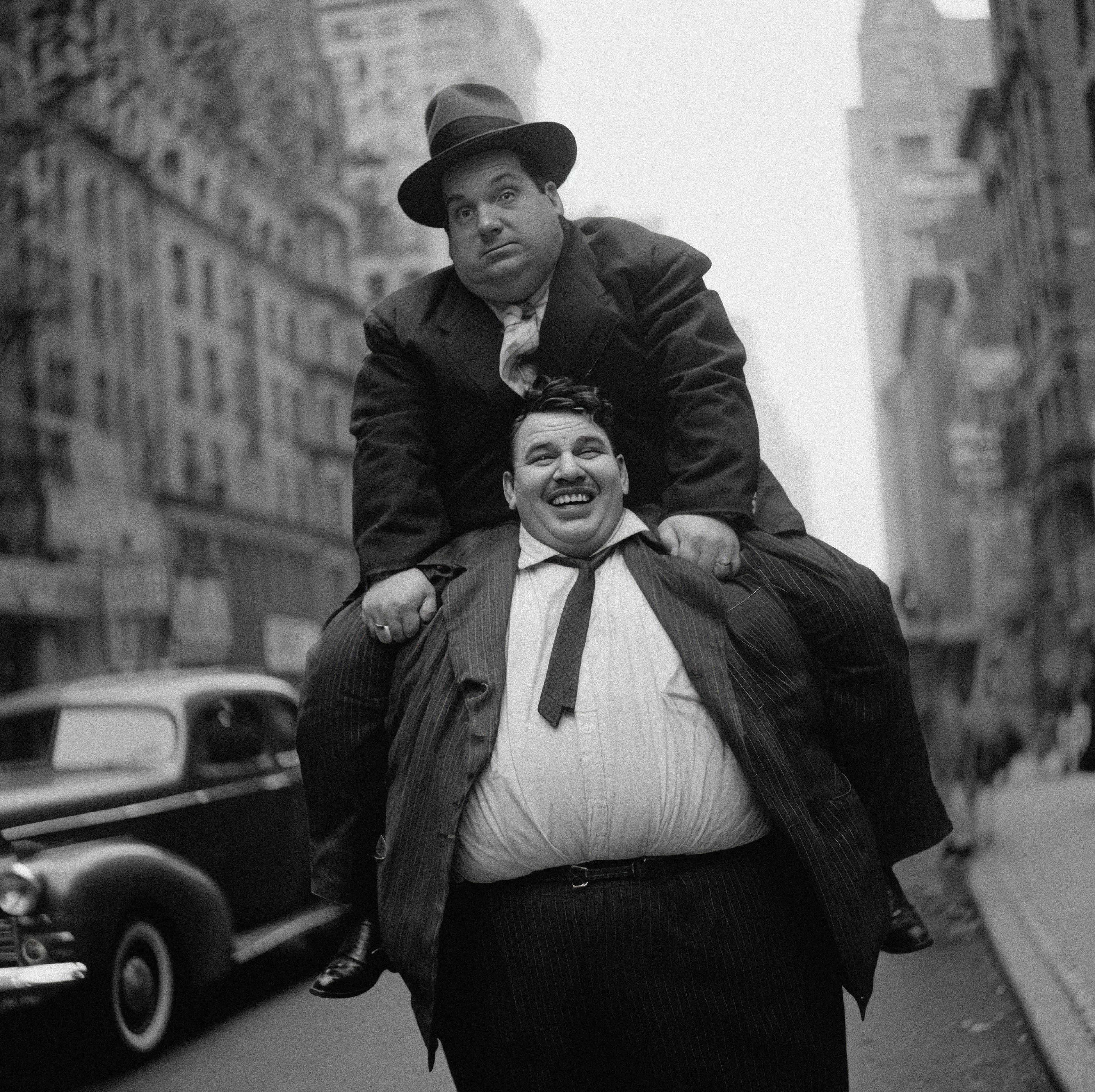 One man sitting on the back of another one wearing suits