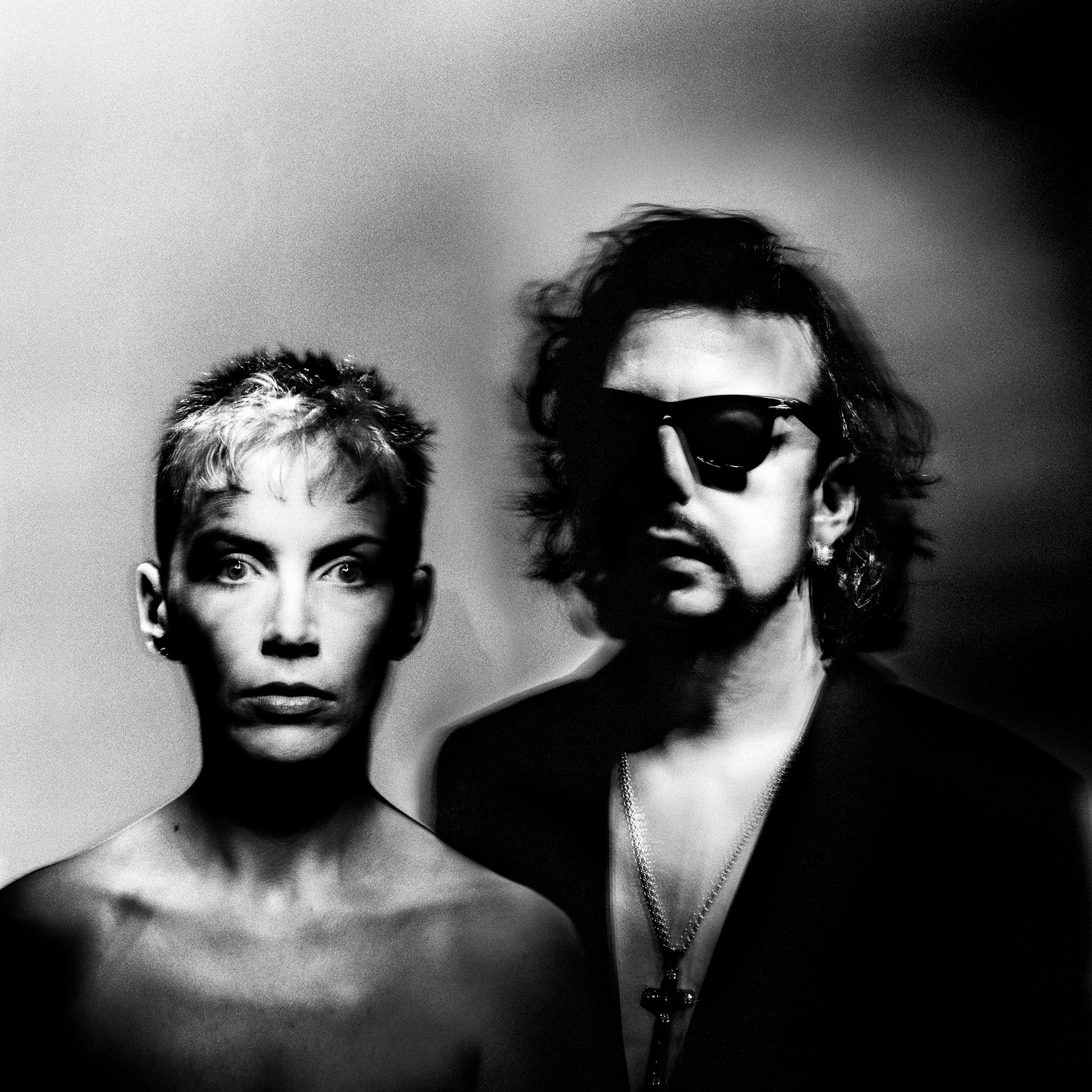 Black image of a woman with short hair and a man with long hair and sunglasses