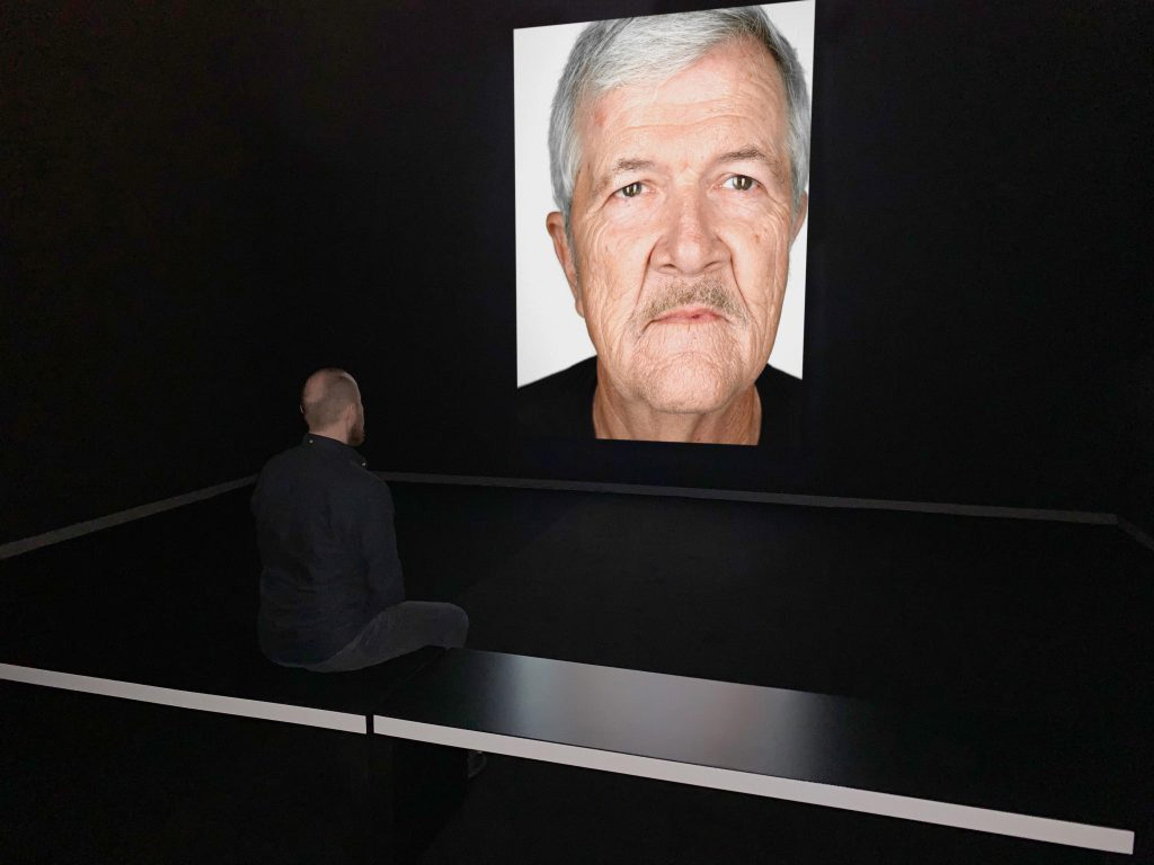 An observer looking at at an image projected in a dark room of a portrait of a man with white hair