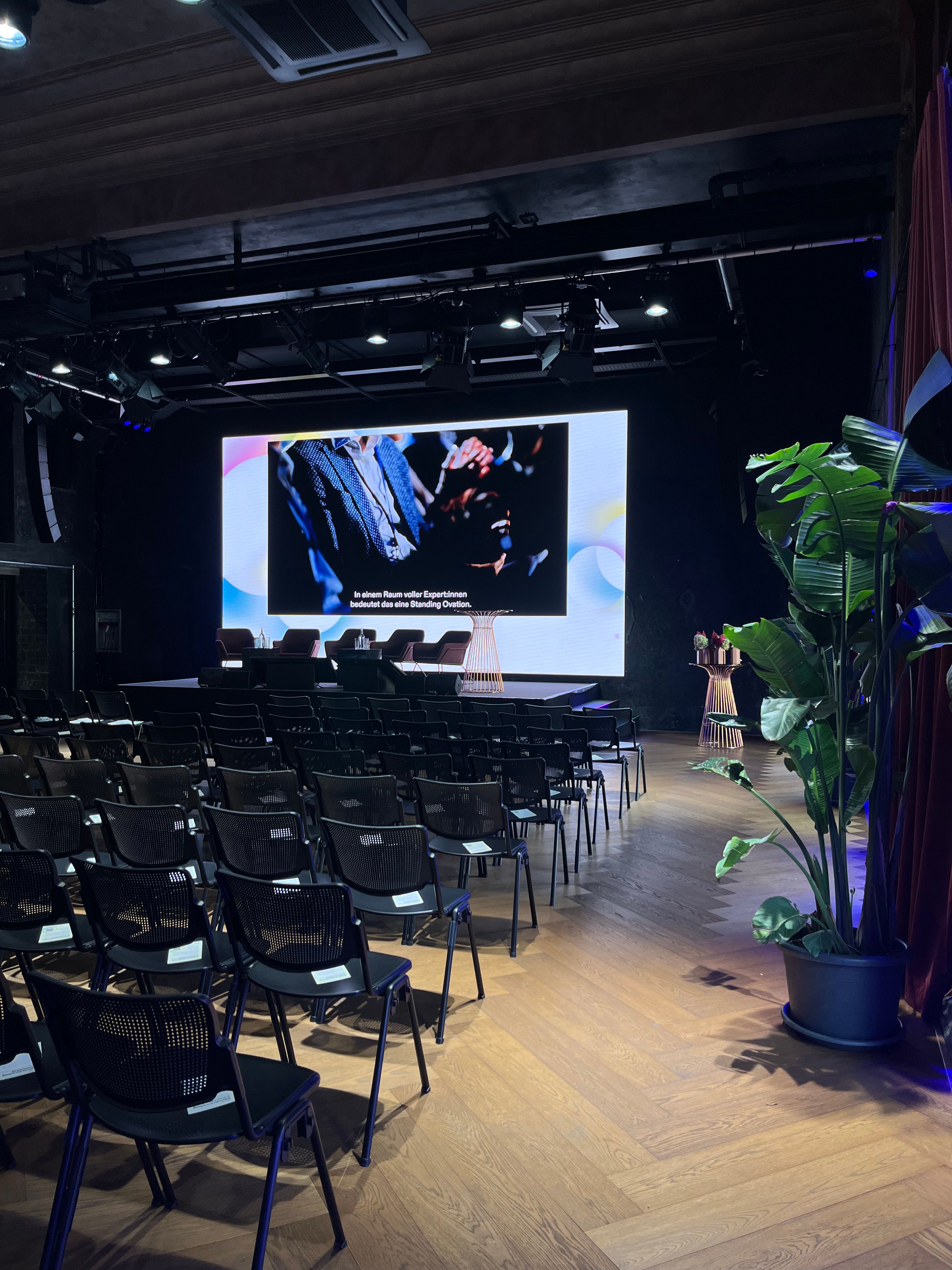 Black chairs in rows, big screen, plant on the right
