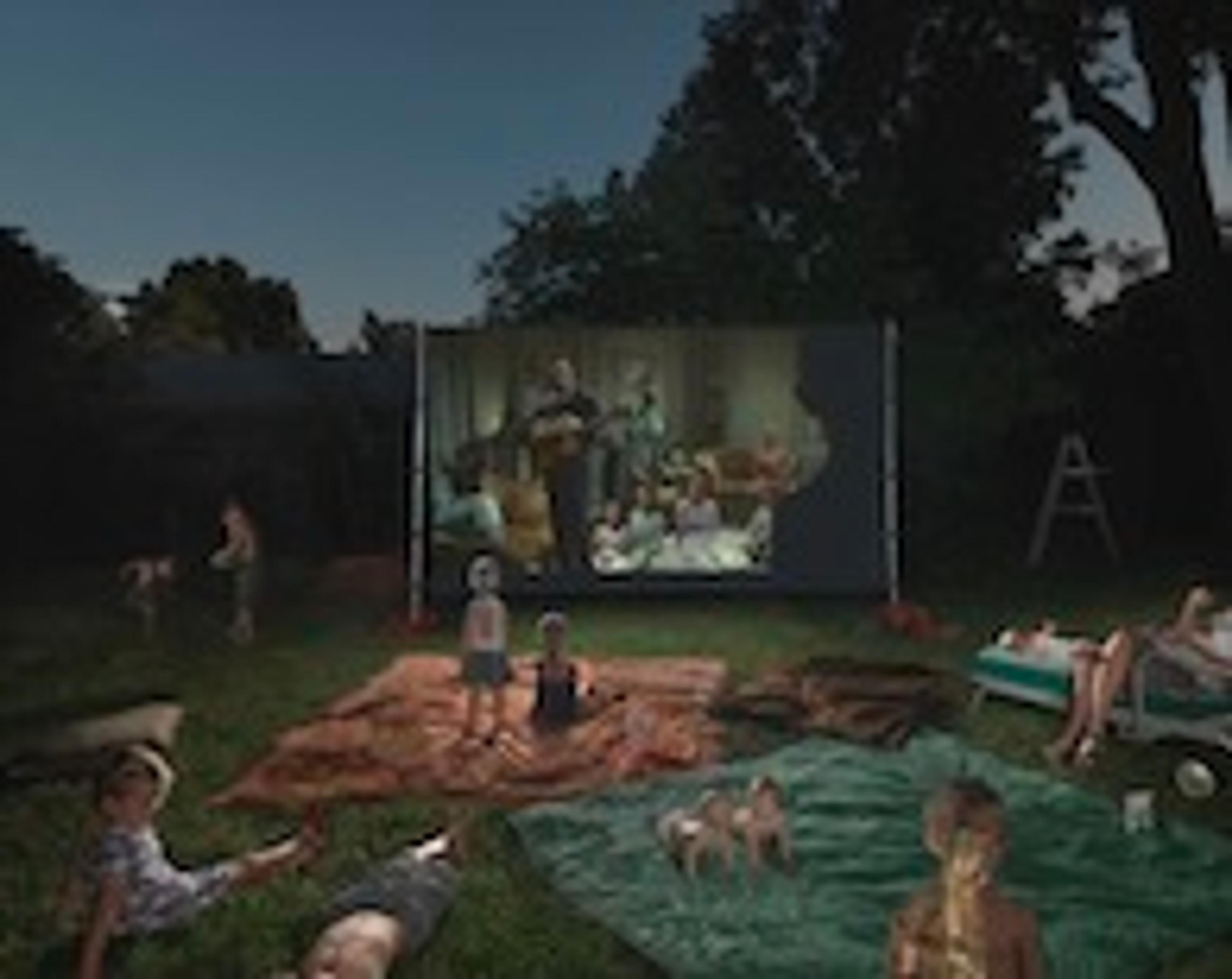 A photograph of several children viewing a movie projected on a screen outdoors