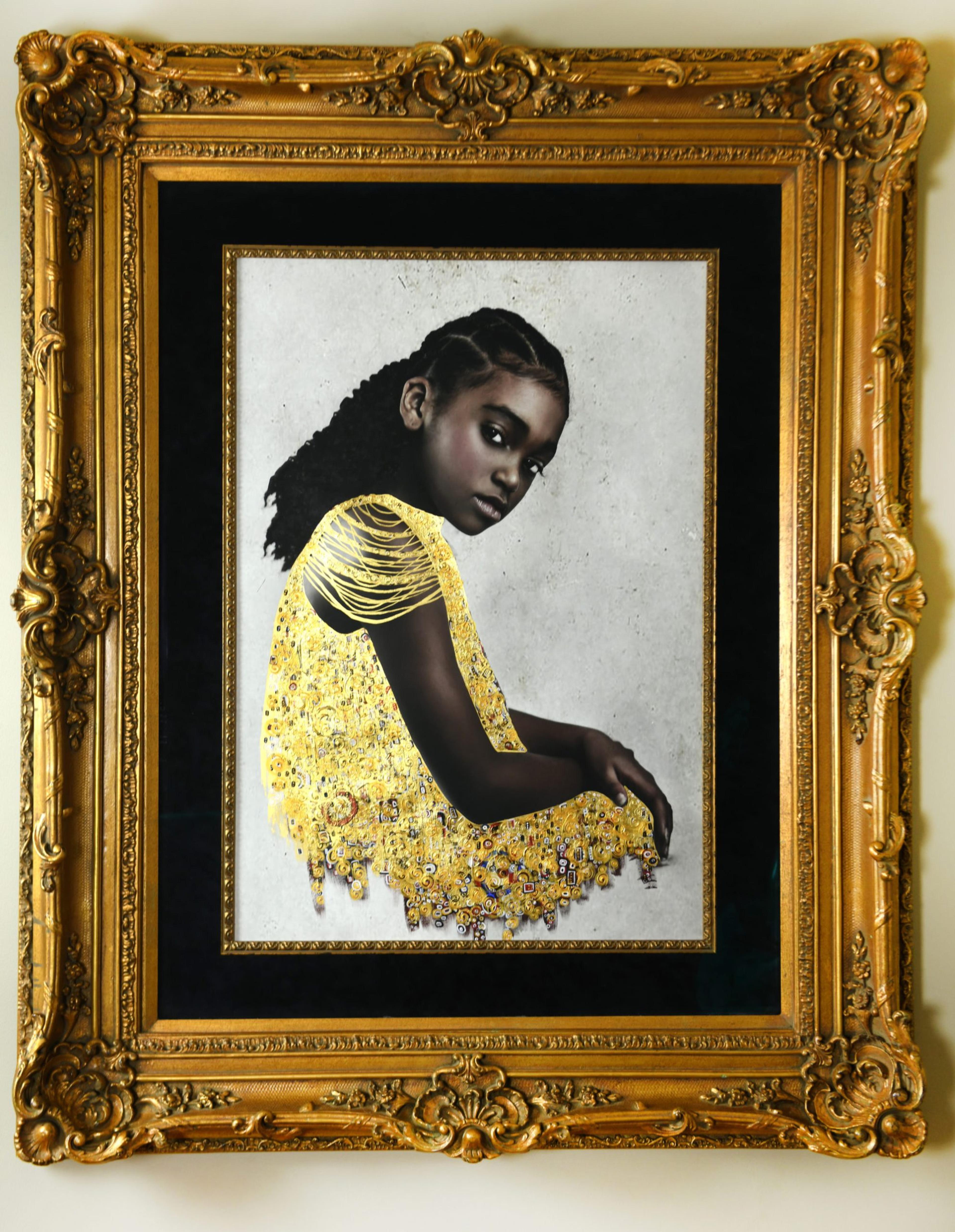 A photograph hanging on a white wall, in a gold ornate frame, of a young girl wearing a yellow dress