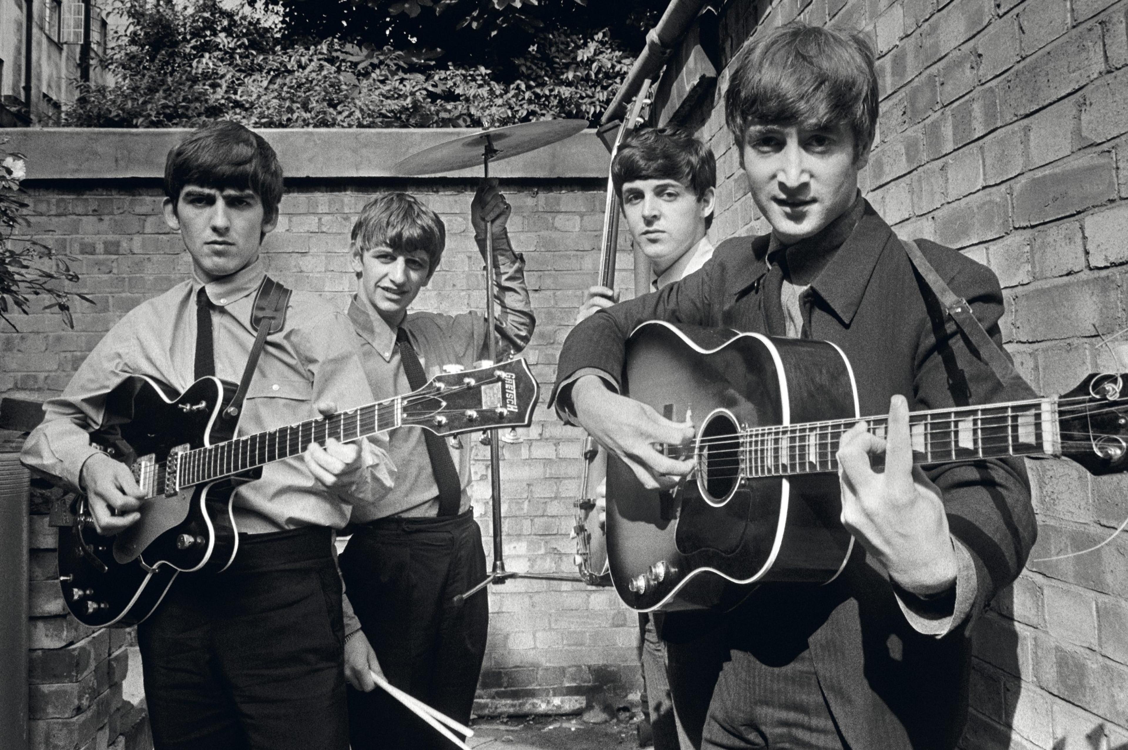 A black-and-white photograph of The Beatles holding their instruments against a brick wall