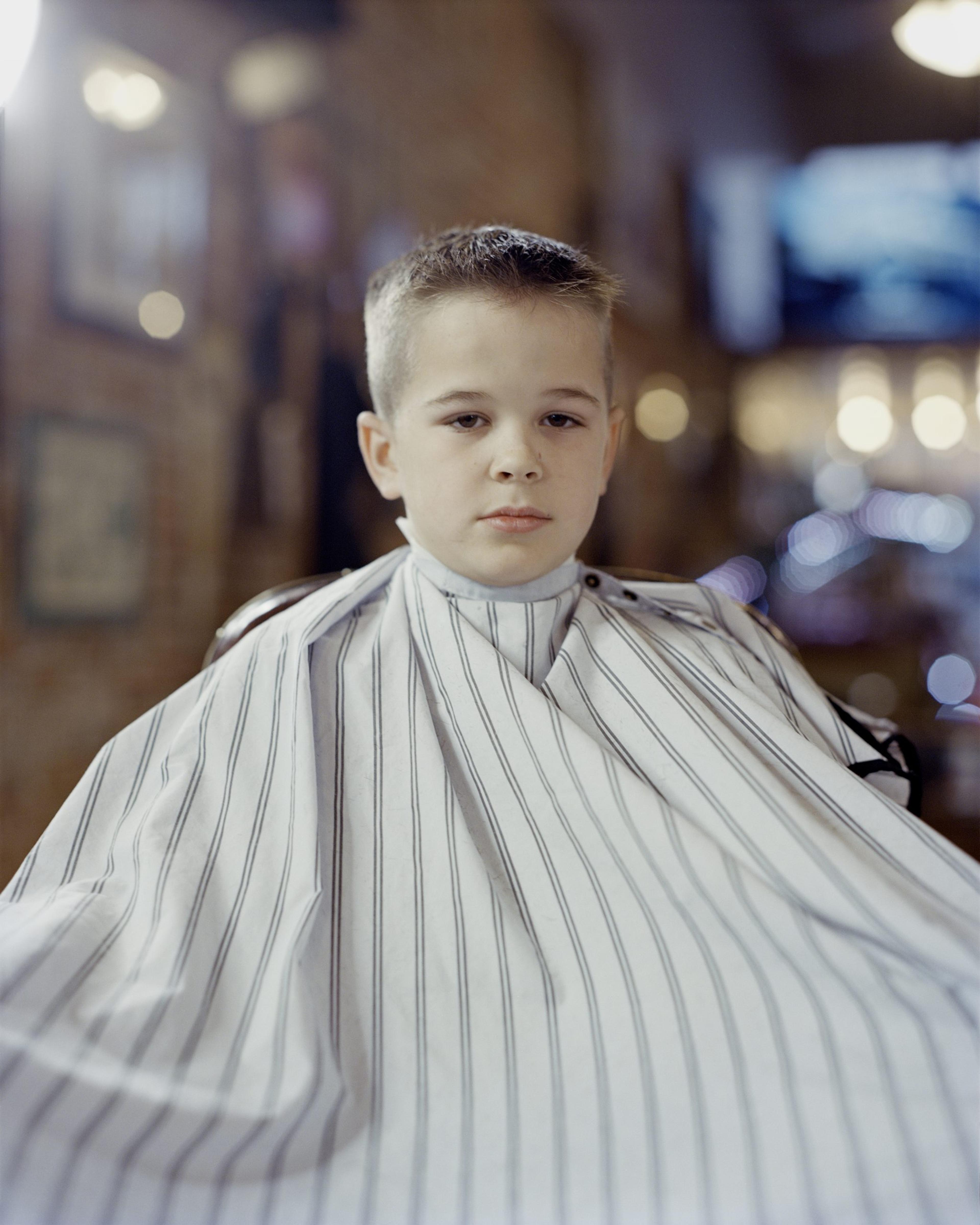 A photograph of a young boy post-haircut, wearing a striped cape.