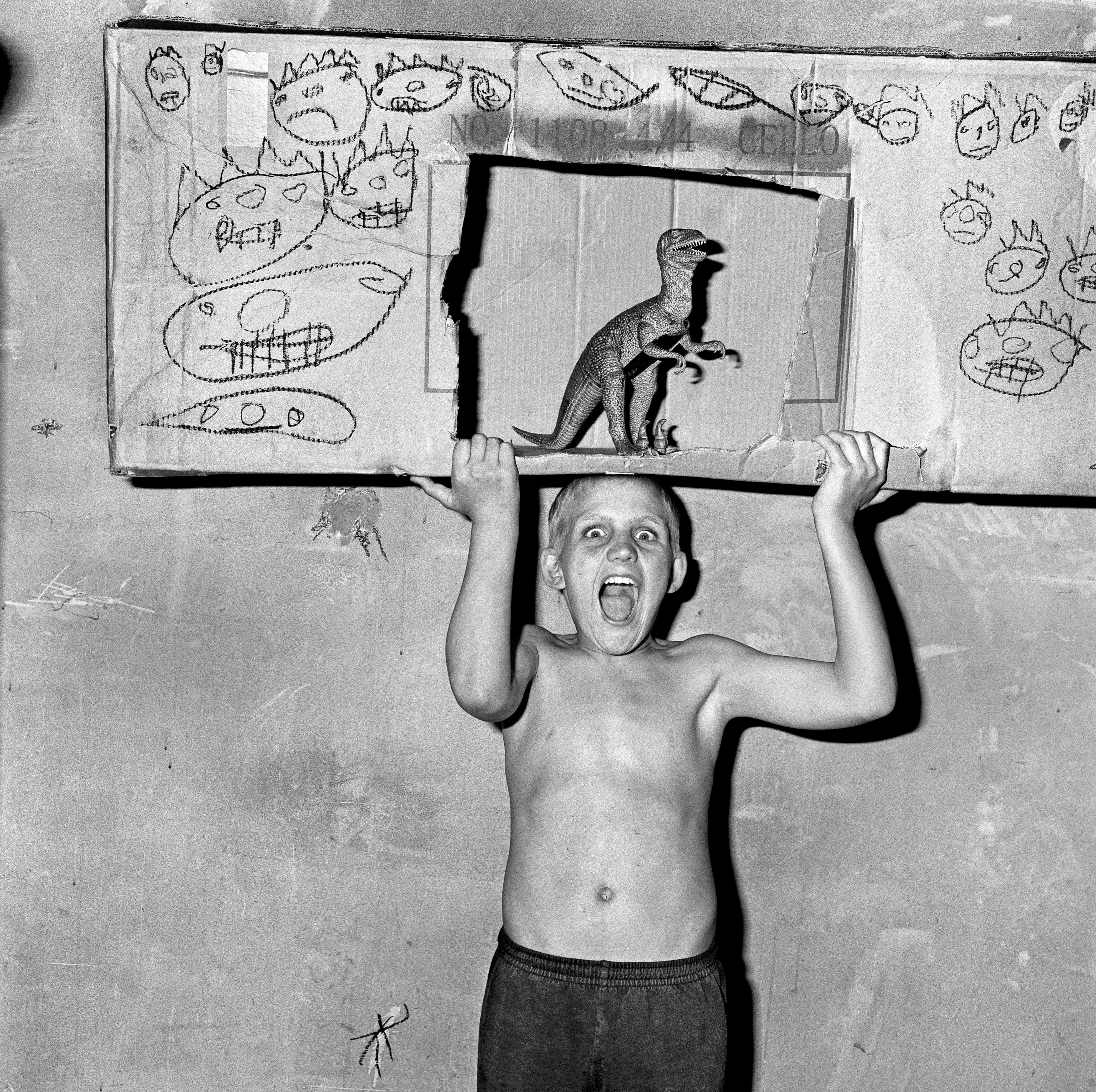 Child holding a cardboard box with drawings and a cut out with a toy dinosaur