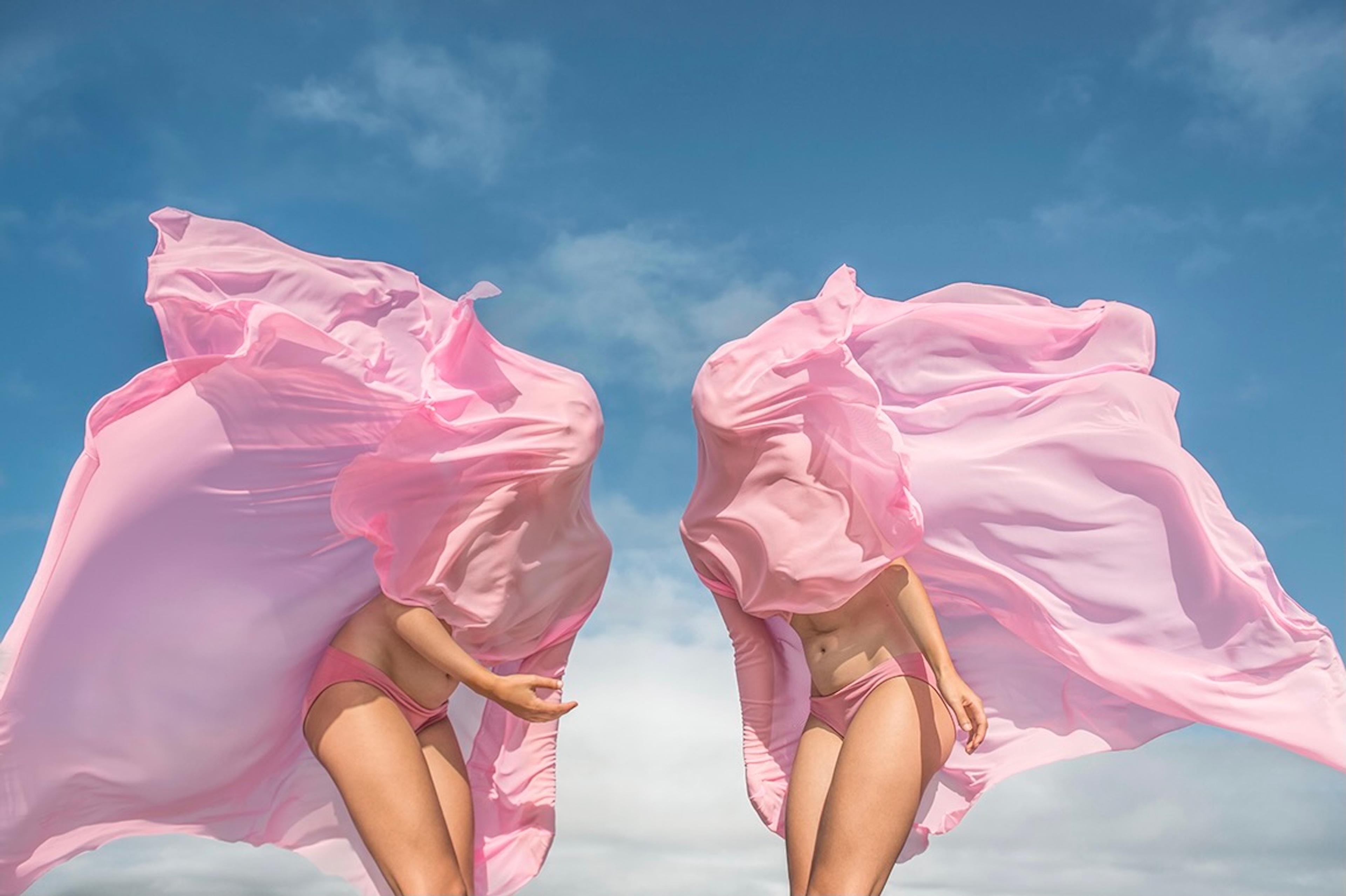 A symmetrical photograph of two women covered in pink sheets from the waist up