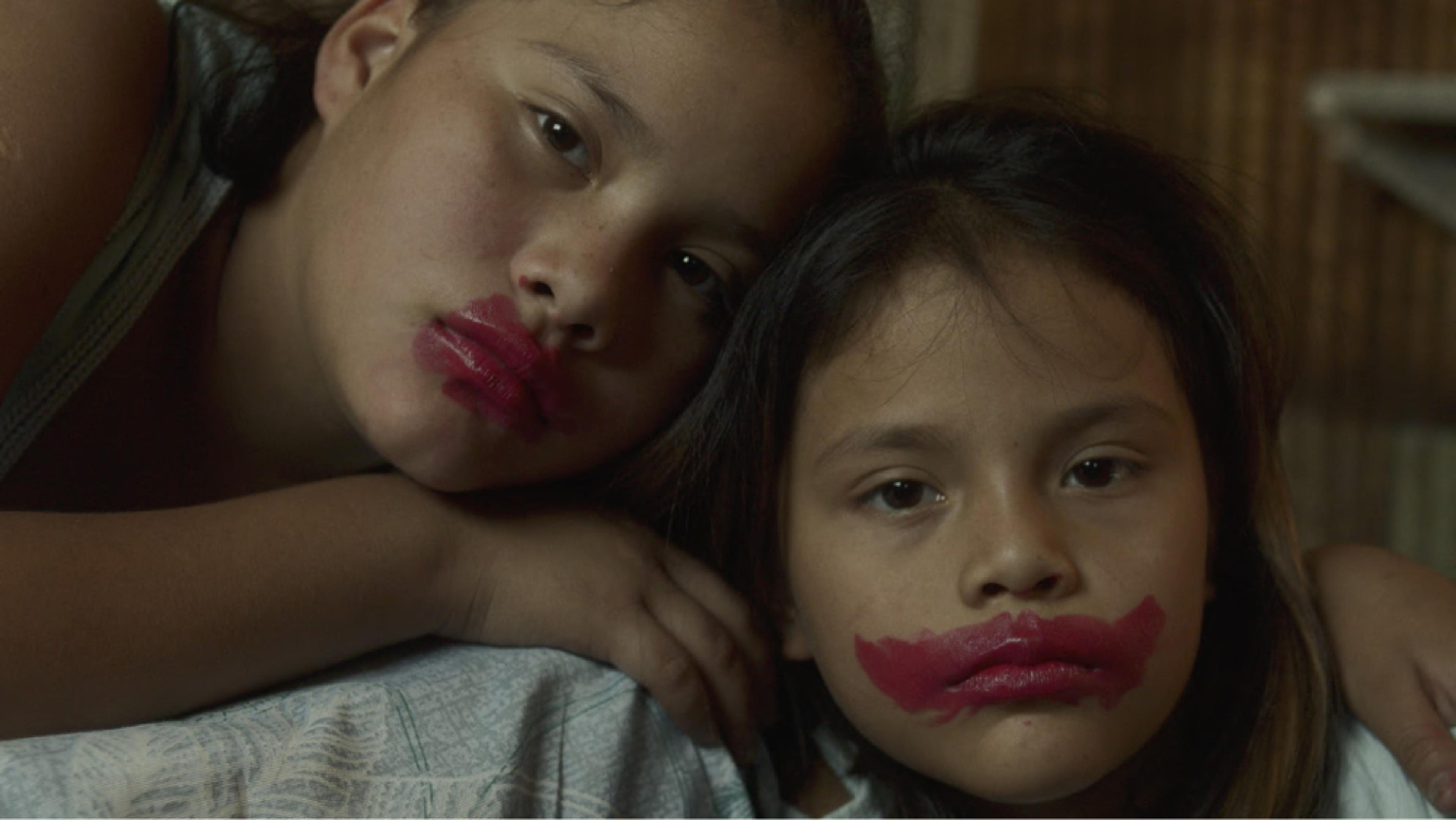 Two kids with lipstic on their lips looking directly to the camera. 