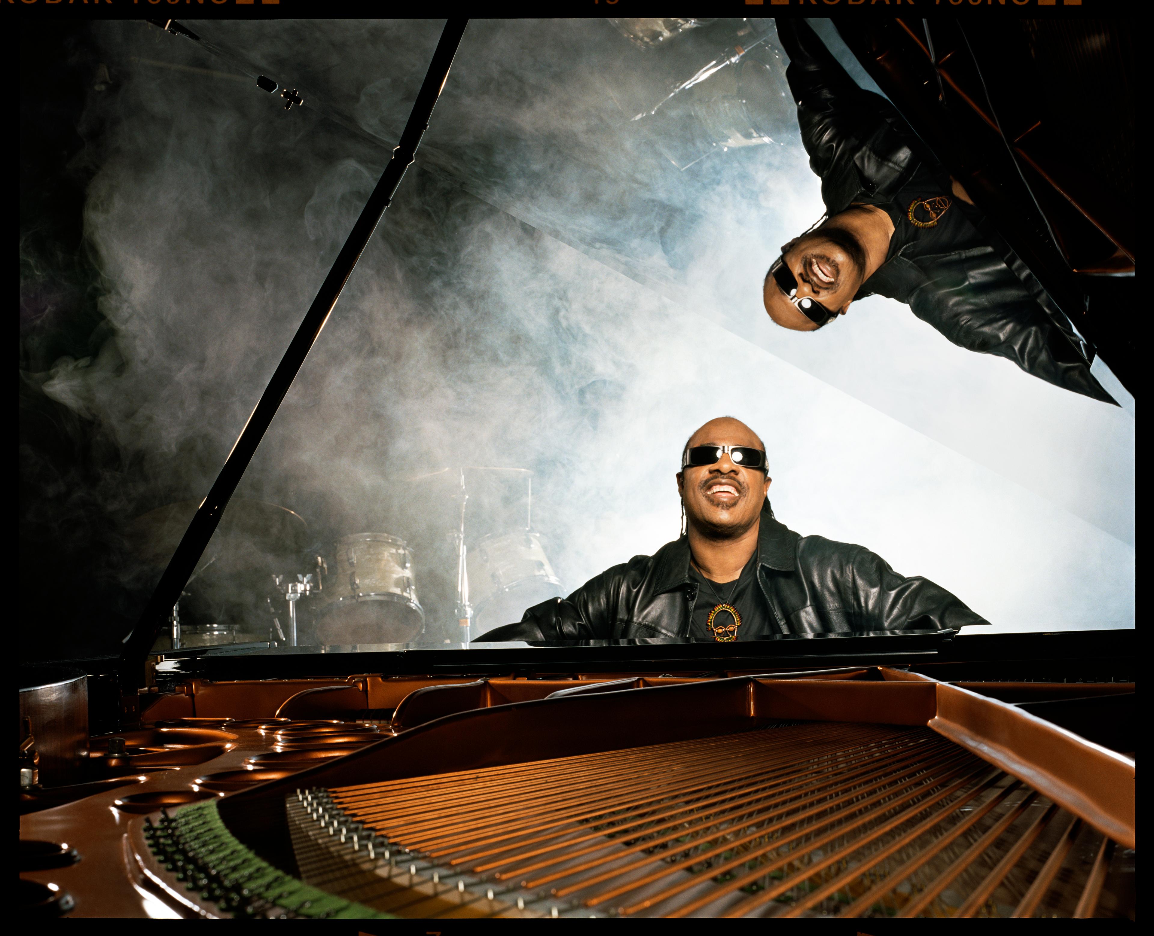 Stevie Wonder playing the piano with his likeness reflected on the piano lid.