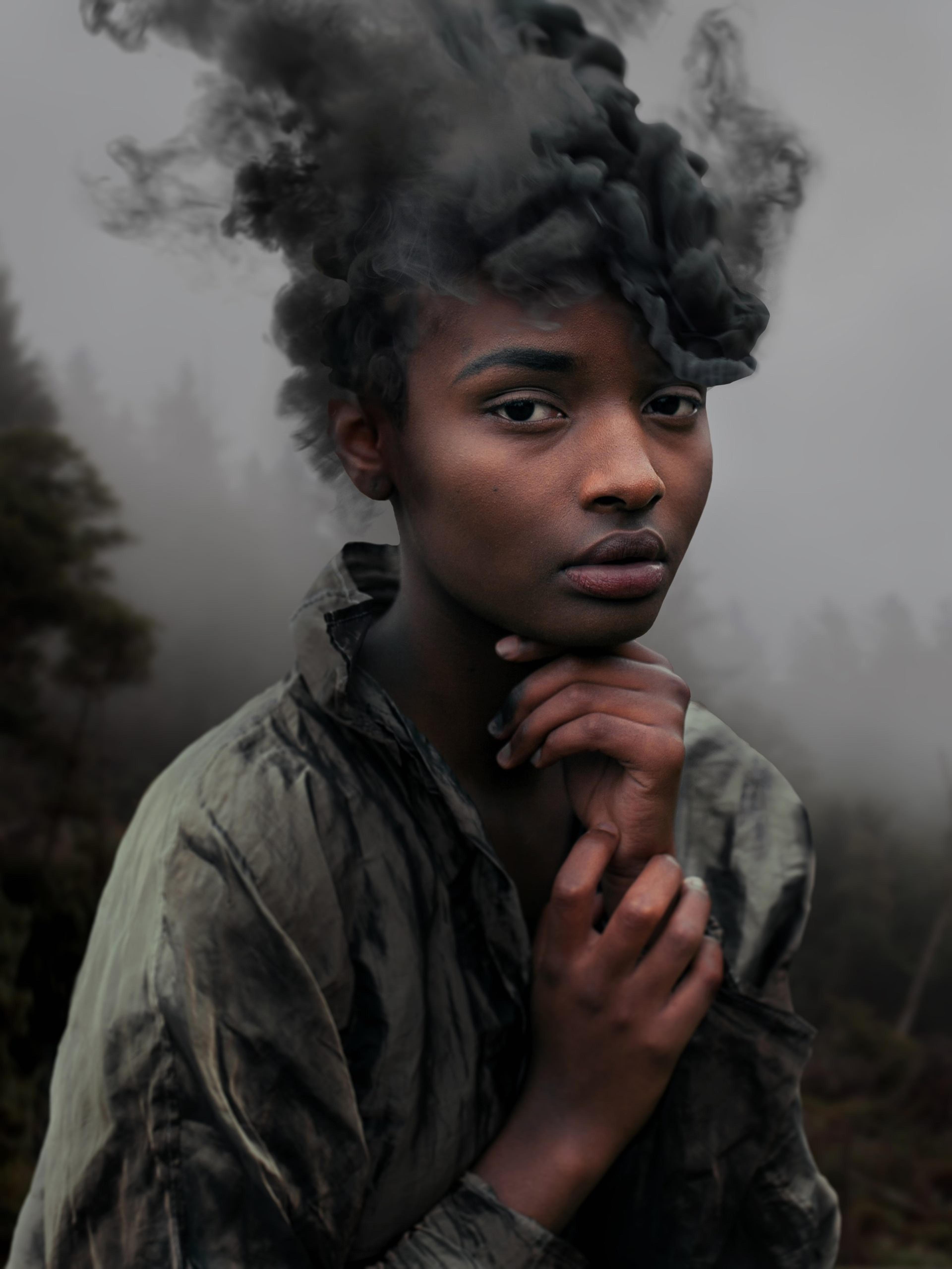A portrait of a woman in a foggy forest with smoking hair looks past the camera