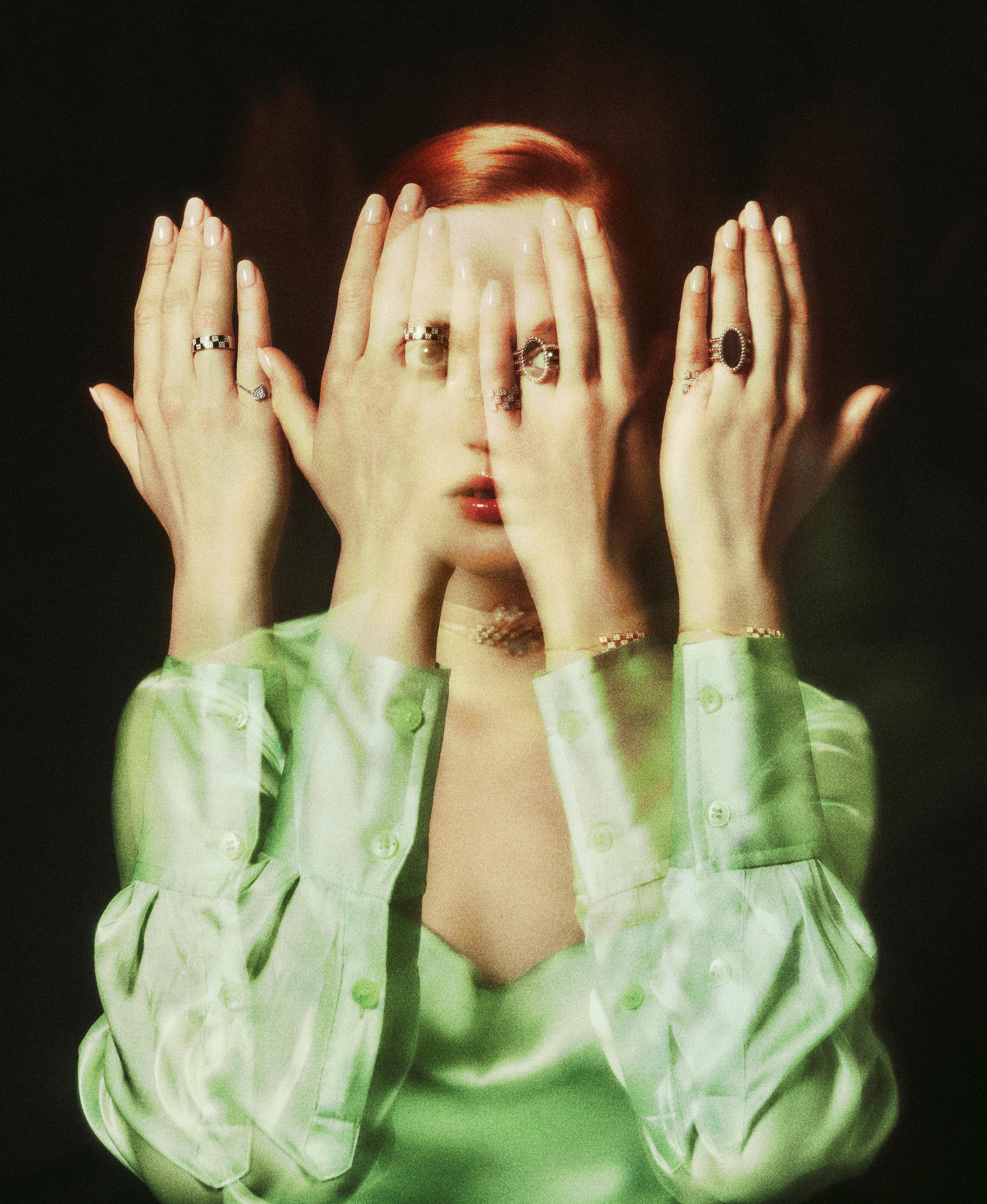 Woman in a green blouse with her hands in front of her face.