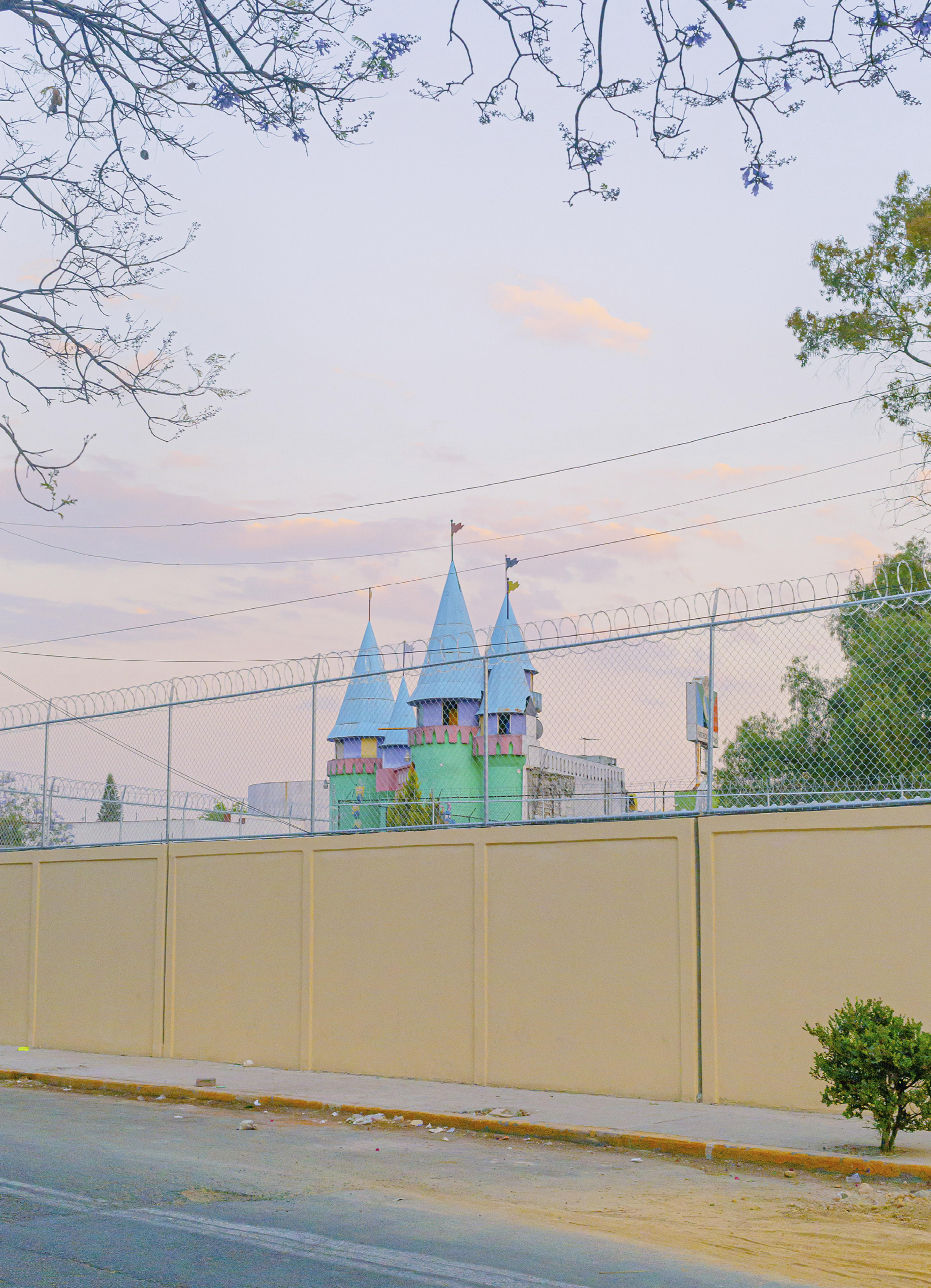 A photograph of a colorful castle against a pastel sky behind a pale yellow fence