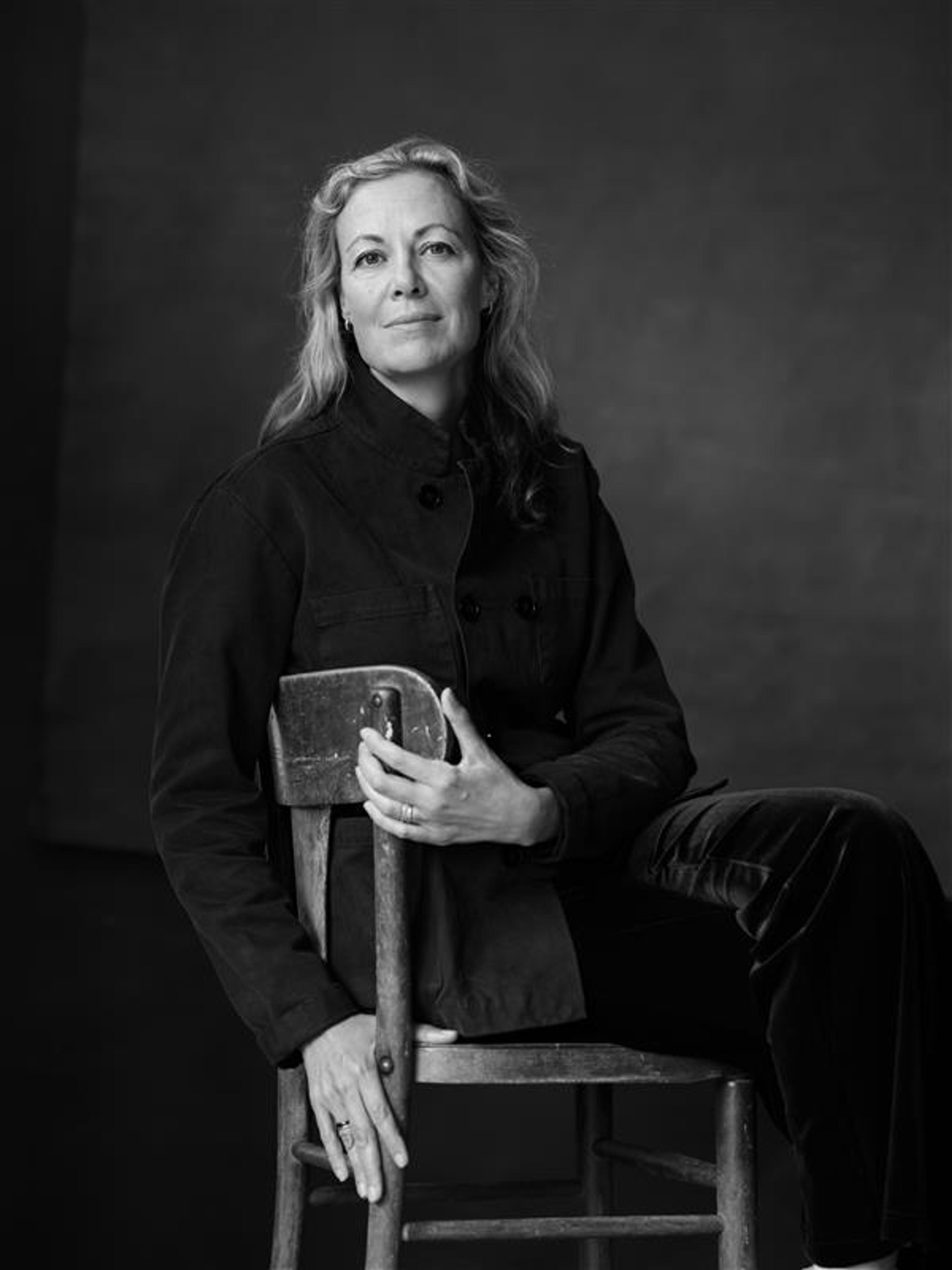 A black and white photo with a woman who is sitting on a wooden chair.