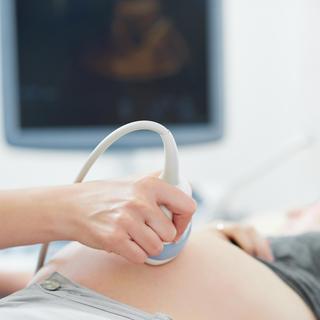 Eine Hand hält eine Ultraschallsonde, die auf den Bauch einer Person gehalten wird.