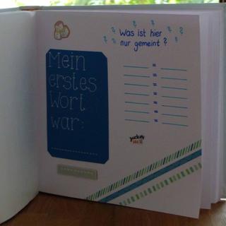 Eine Seite aus einem Notizbuch mit blauem Hintergrund, auf der eine Liste mit der Überschrift "Mein erstes Wort war:", gefolgt von einer Liste von Wörtern und einer kleinen Illustration eines Menschen und eines Hundes zu sehen ist.