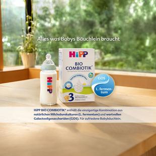 Packung HiPP Bio Combiotik 3 Babynahrung steht auf einem Holztisch vor einem Fenster mit Pflanzen im Hintergrund