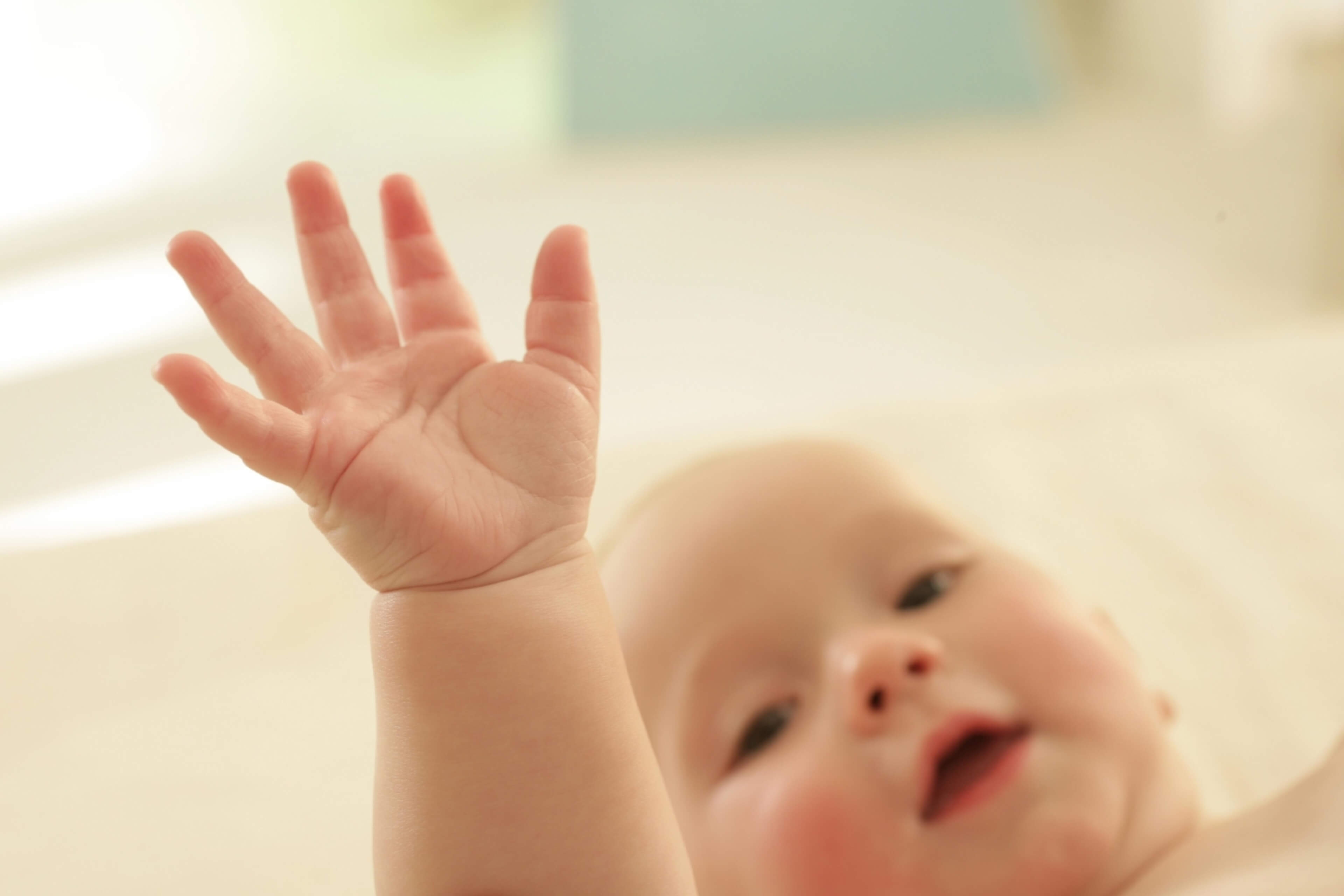 Ein Baby mit erhobener Hand und konzentriertem Blick auf die Kamera.