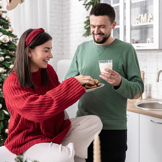 Expecting couple sat in front of the Christmas tree eating cookies