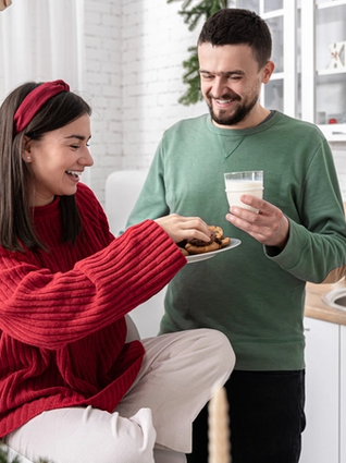 Expecting couple sat in front of the Christmas tree eating cookies