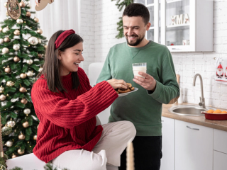 Expecting couple sat in front of the Christmas tree eating cookies