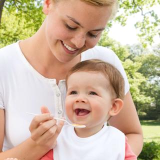 Ein freudiger Moment zwischen einer Mutter und ihrem Baby, bei dem die Mutter ihr Kind mit einem Löffel füttert.