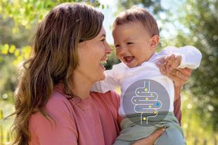 Lachende Mutter hält ihr Baby im Grünen, auf dem Bauch des Kindes ist eine stilisierte Darmgrafik für eine gesunde Darmflora eingeblendet.