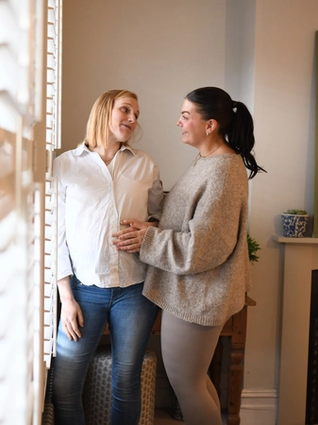 Expecting couple looking at each other playfully whilst both touching bump
