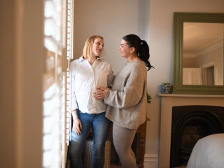 Expecting couple looking at each other playfully whilst both touching bump