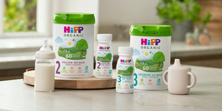 HiPP Organic follow on and growing up milks on a kitchen worktop next to a bottle of milk and a sippy cup