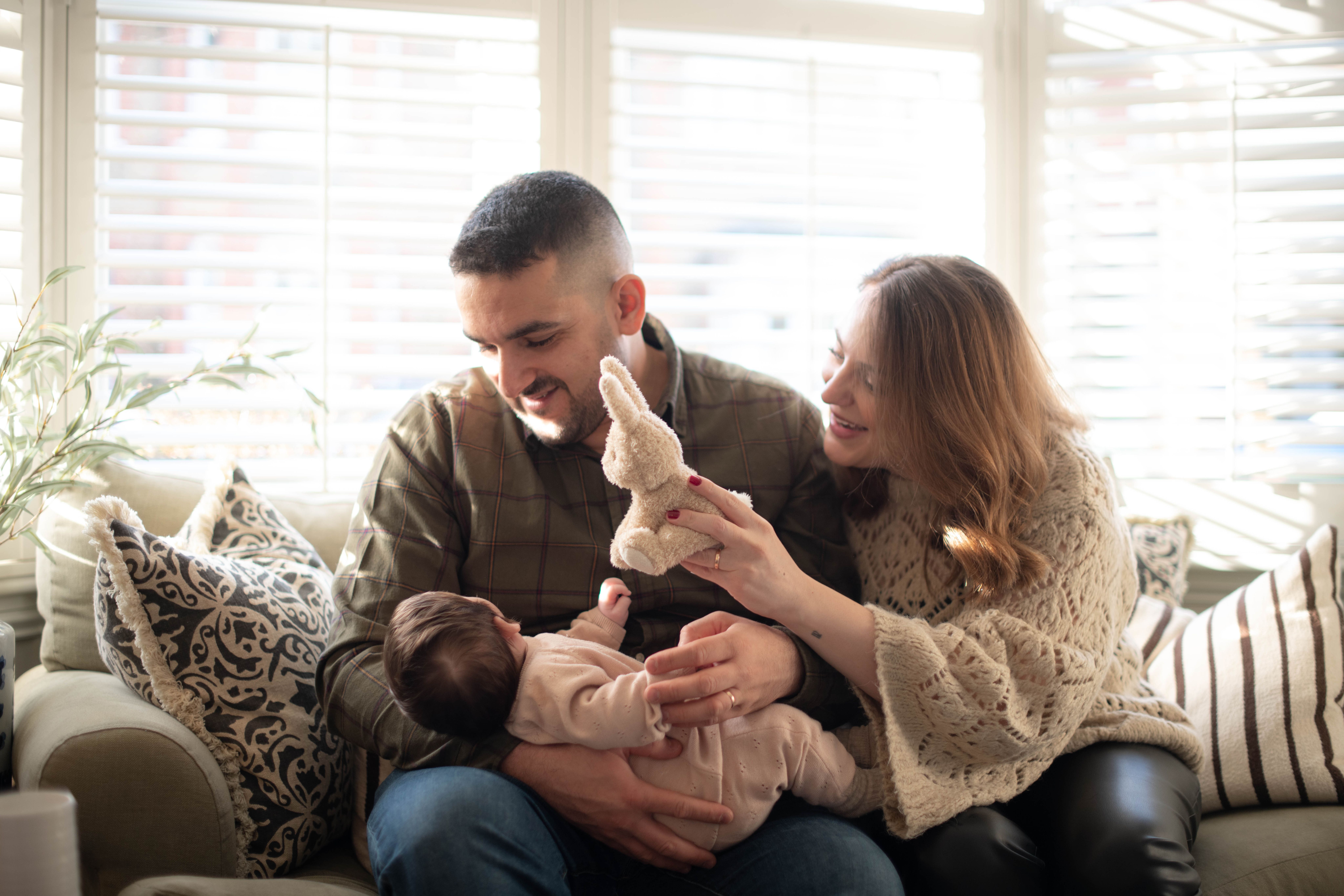Mum and dad cuddling their baby on a sofa in a living room