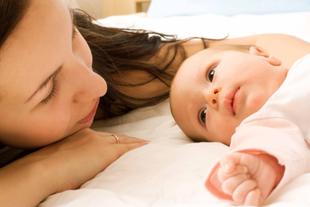 Ein zärtlicher Moment zwischen einer Mutter und ihrem Baby, in dem die Mutter das Baby sanft anschaut, während beide auf einem Bett liegen.