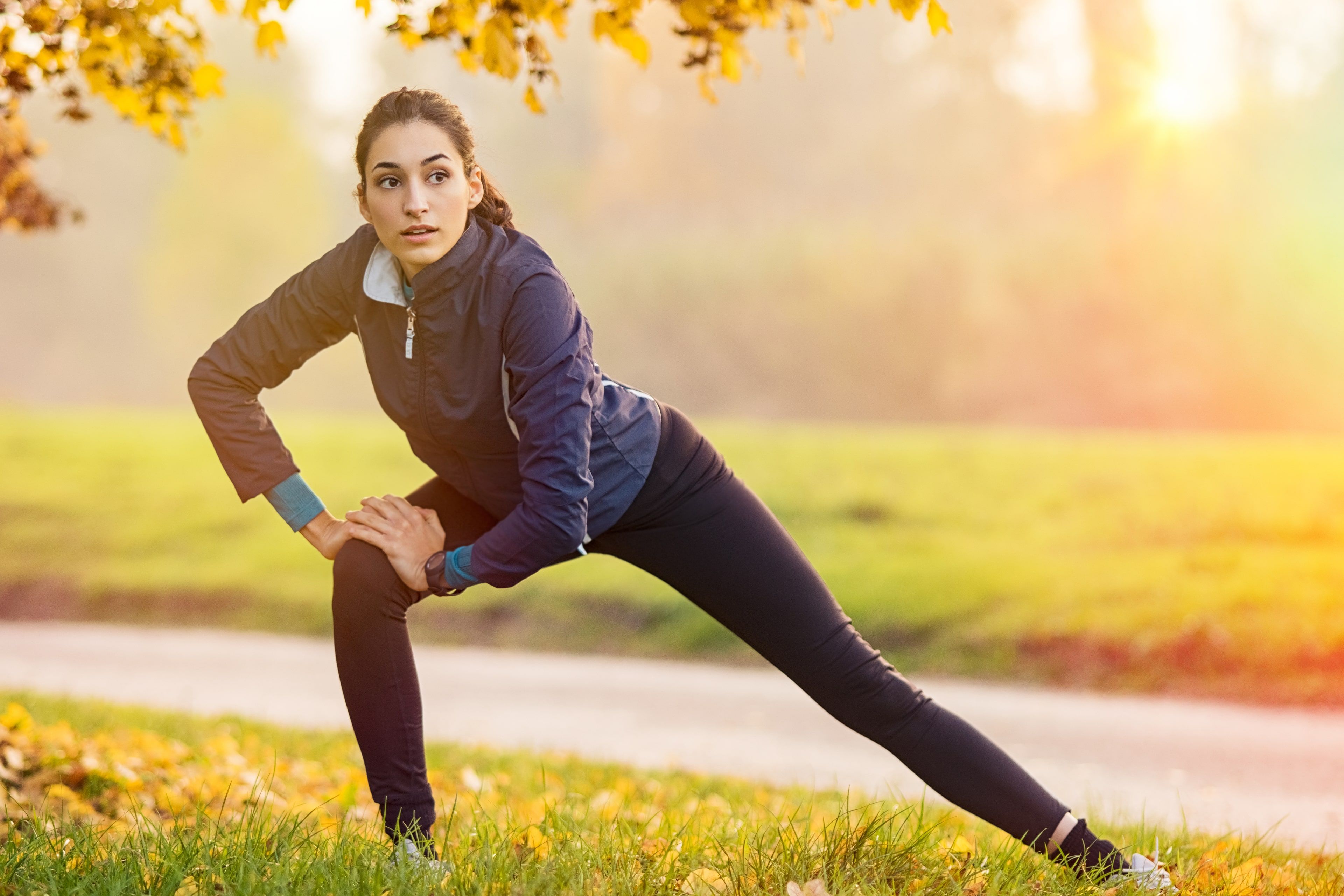 Eine Frau in Sportkleidung dehnt sich im Herbst in einem Park.
