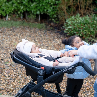 Baby wrapped up warm in pram whilst mum is walking with her toddler at her side
