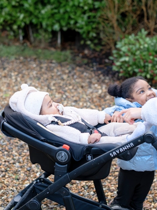 Baby wrapped up warm in pram whilst mum is walking with her toddler at her side