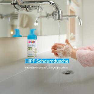 Kind wäscht Hände unter fließendem Wasser neben einer Flasche HiPP Schaumdusche auf dem Waschbecken
