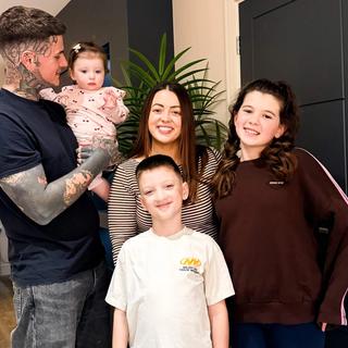 Connor and Charlotte smiling at home with their three young children, capturing a happy family moment