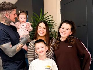 Connor and Charlotte smiling at home with their three young children, capturing a happy family moment