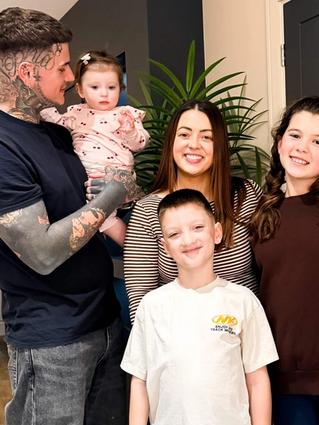 Connor and Charlotte smiling at home with their three young children, capturing a happy family moment