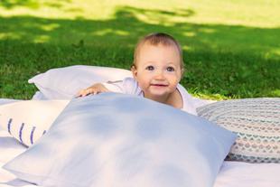 Ein Baby, das auf einer weißen Fläche liegt, umgeben von grünem Gras, mit einem hellen und fröhlichen Gesichtsausdruck.