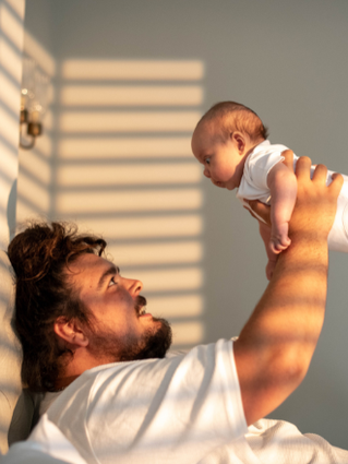 Dad playing with newborn baby infront of window