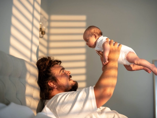 Dad playing with newborn baby infront of window