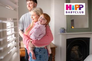 Mum and dad holding their toddler, looking out a window in their living room
